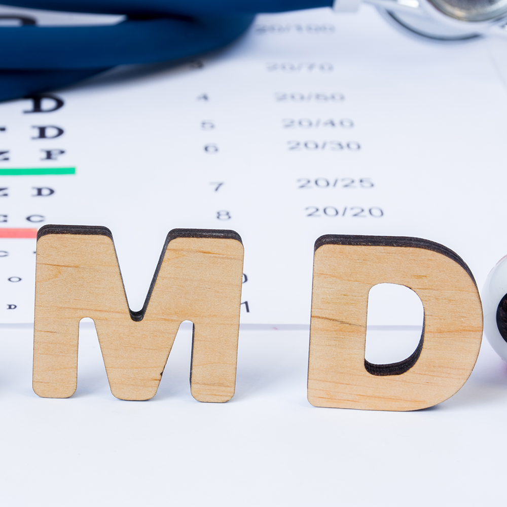 AMD Abbreviation or acronym of age-related macular degeneration - eye problem in older persons. Word AMD is on foreground near eye model with stethoscope and visual acuity test on blurry background